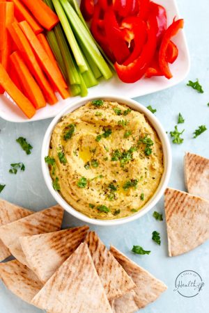 roasted garlic hummus in a white bowl with pita bread and veggie sticks