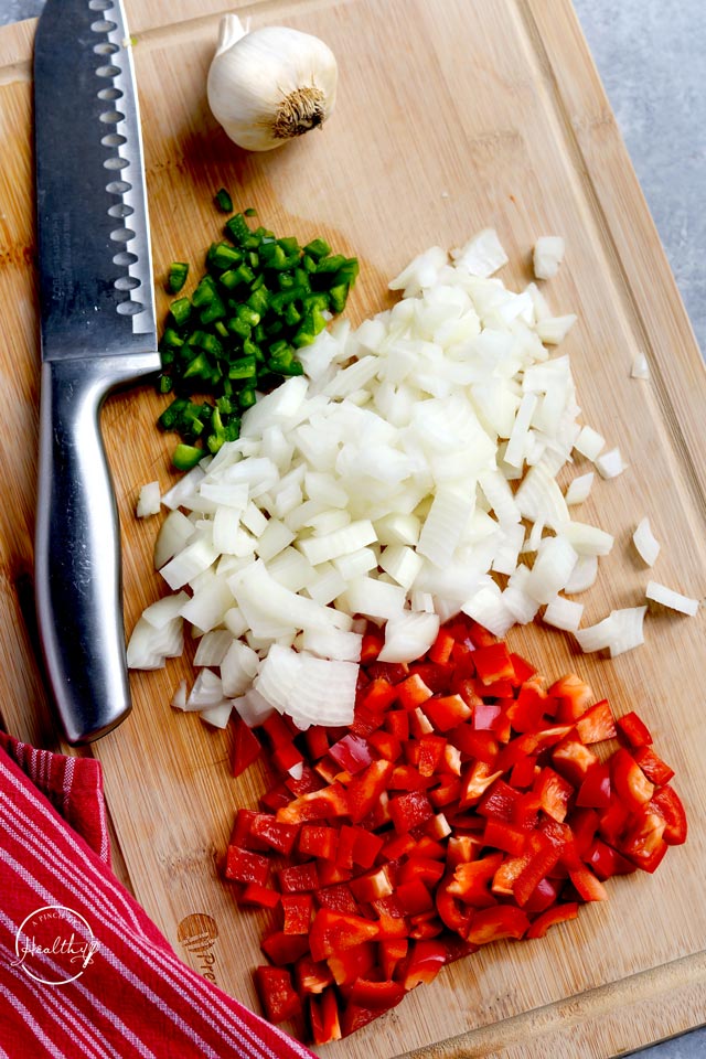 Diced onions and peppers with knife on wood cutting board