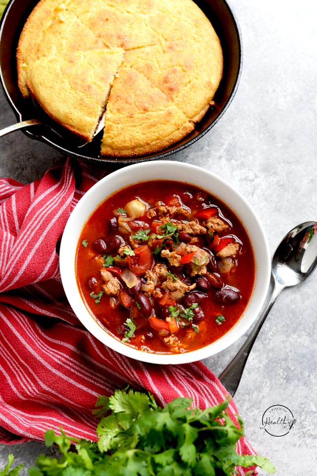 Instant Pot turkey chili in white bowl with cornbread and red towel