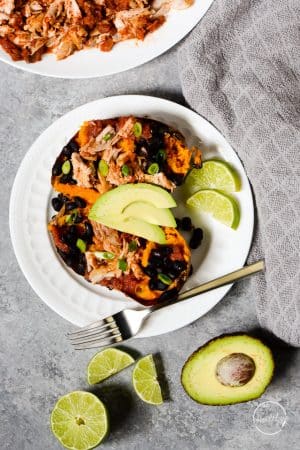 sweet potato with chicken, black beans, avocado and green onion on white plate with a fork