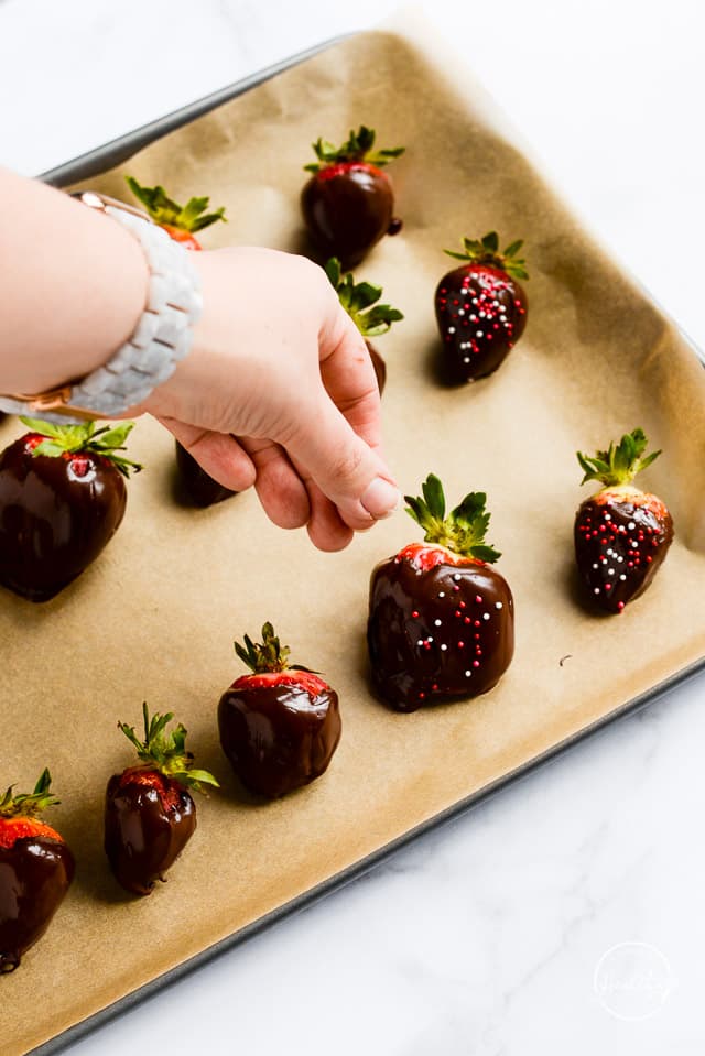 hand dropping sprinkles on dark chocolate dipped strawberries