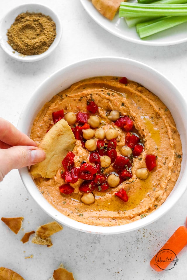hand dipping pita bread in roasted red pepper hummus