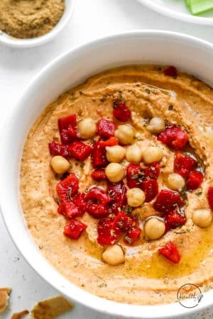 roasted red pepper hummus shot closeup in a white bowl with chickpea and red pepper garnish