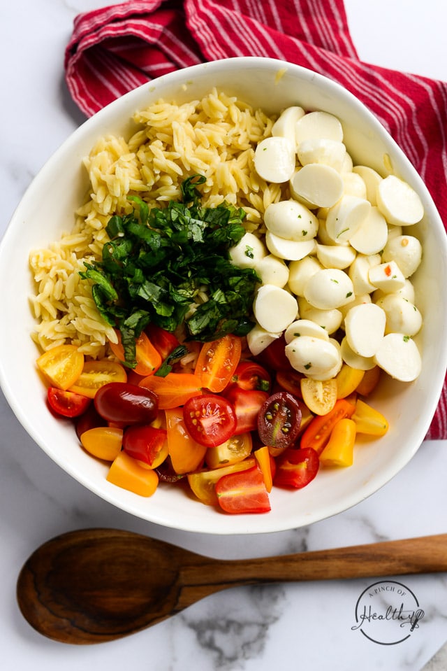 orzo pasta, basil, fresh mozzarella, rainbow tomatoes in a white bowl
