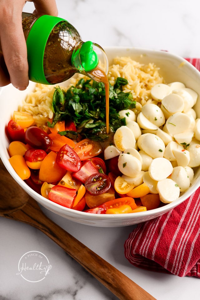 pouring balsamic vinaigrette on caprese pasta salad