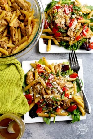 Greek chicken pasta on square white plates with tomato, feta and basil