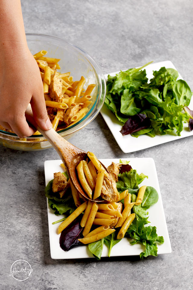 spooning greek chicken pasta onto greens