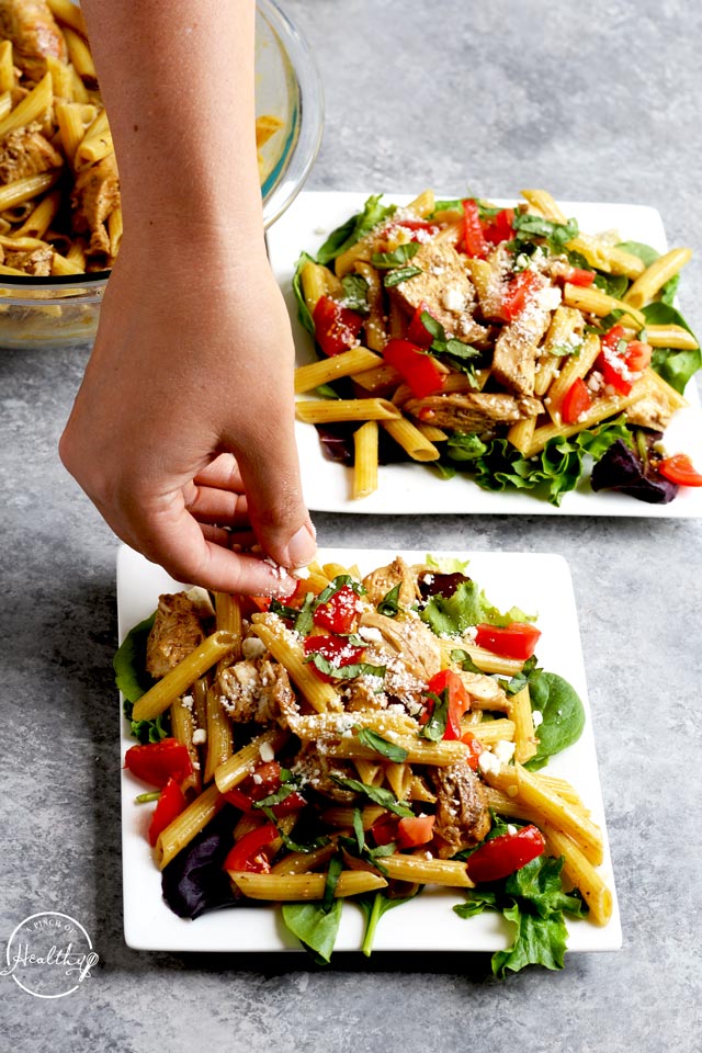 Greek chicken pasta with hand sprinkling feta cheese crumbles on top