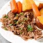Classic pot roast with carrots and potatoes on a white plate closeup