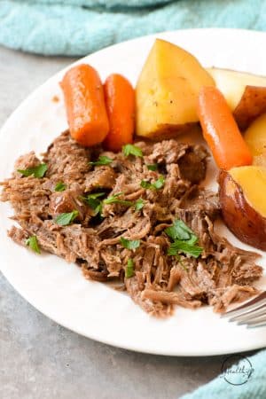 Classic pot roast with carrots and potatoes on a white plate closeup