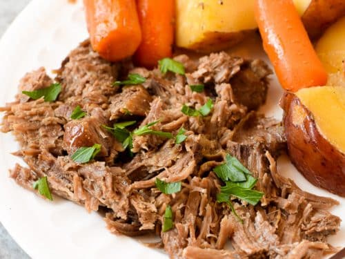 Classic pot roast with carrots and potatoes on a white plate closeup