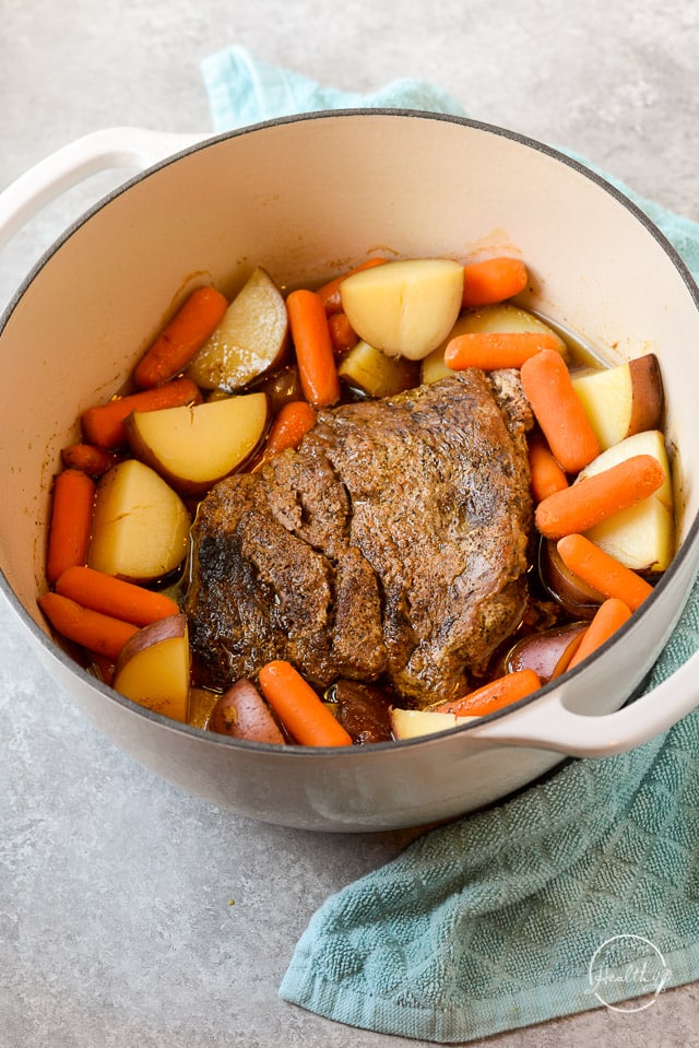 Classic pot roast in white enameled Dutch oven with carrots and potatoes