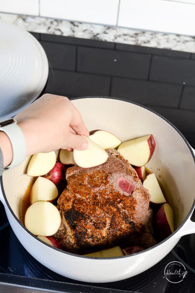 hand adding potatoes to Dutch oven with seared beef