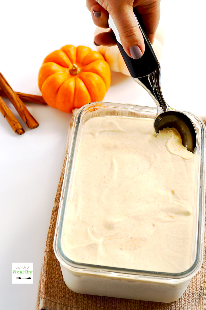 Woman's hand scooping ice cream with pumpkin and cinnamon sticks in the background