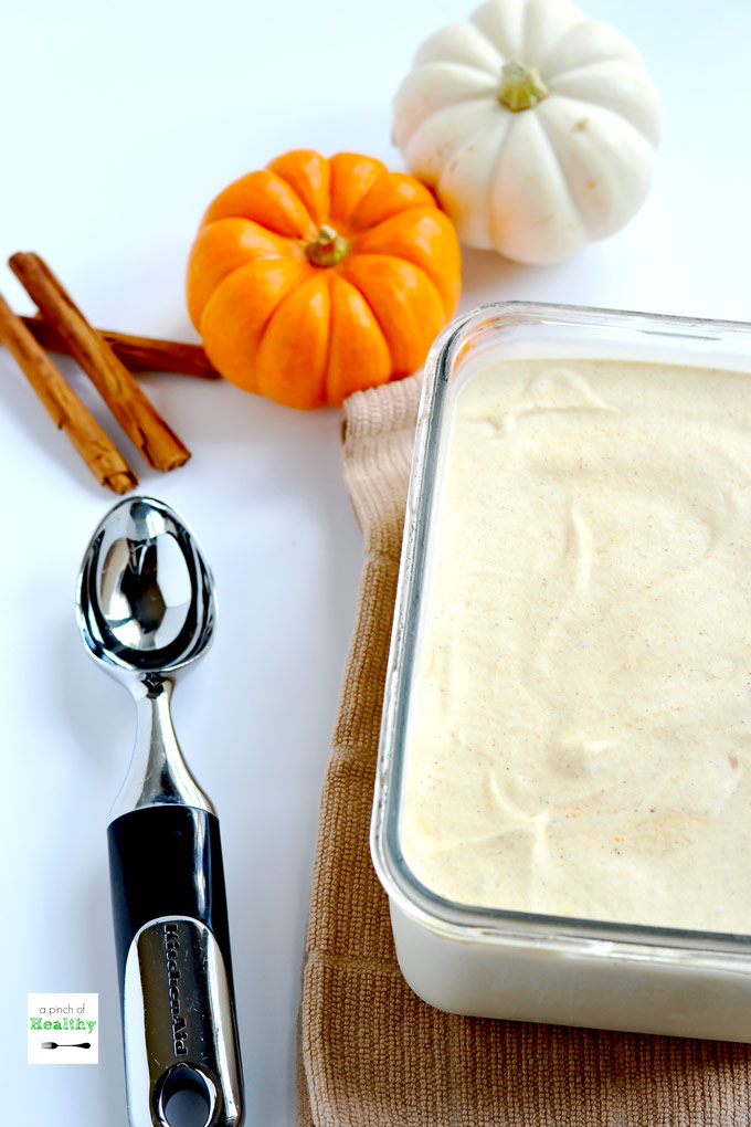 Large rectangle dish of pumpkin ice cream with ice cream scoop and pumpkins on white counter