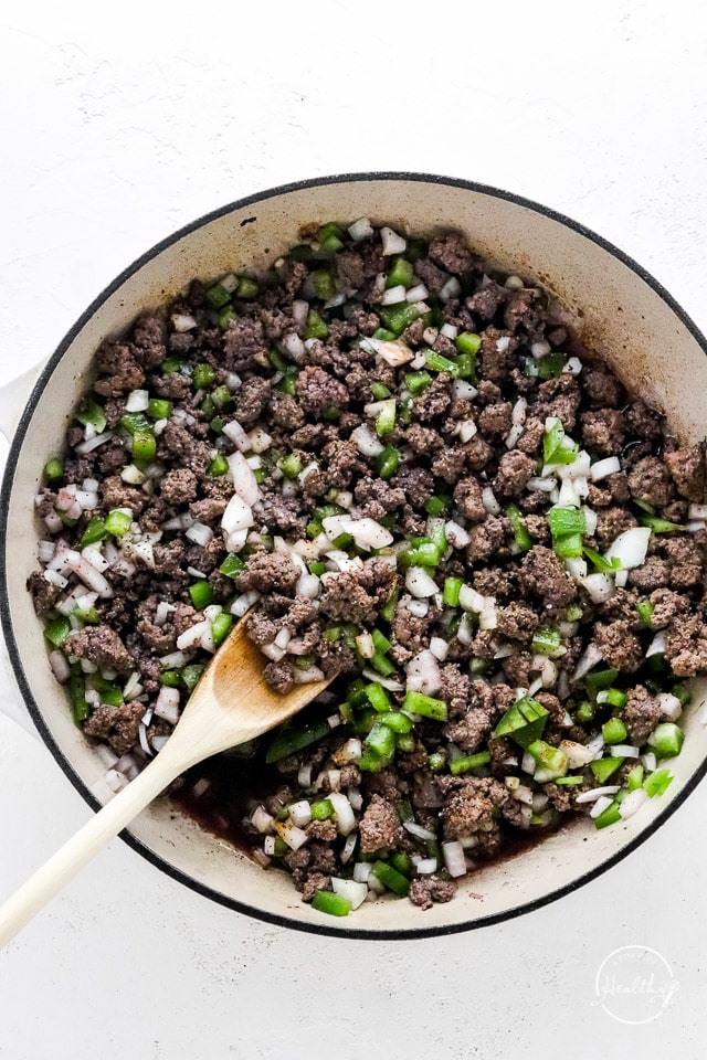 stirring meat, veggies and spices cooking in a big pot with a wooden spoon