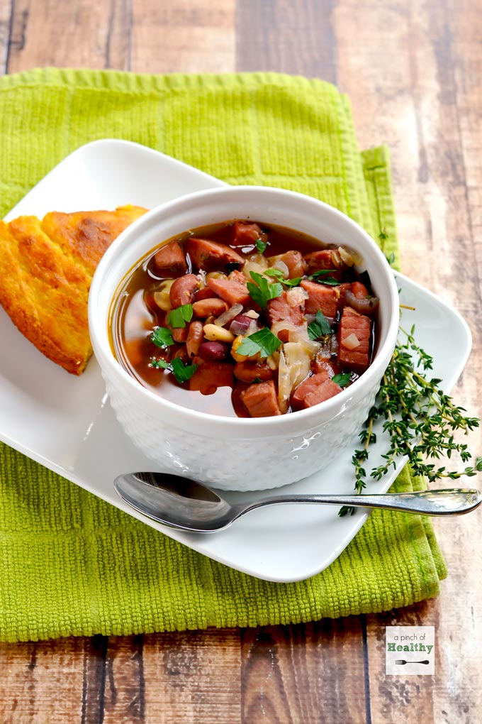 15 bean soup in a white bowl with a side of corn bread on a wood surface with green towel