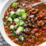 classic beef chili topped with avocado in a white bowl with spoon