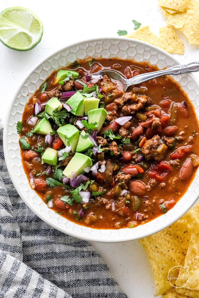 best chili recipe ever in a white bowl with spoon and diced avocado