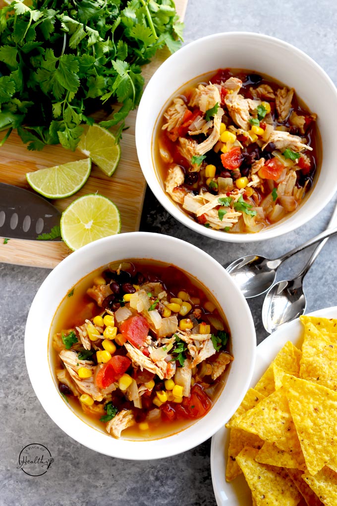 Instant Pot chicken tortilla soup in two white bowls shot overhead with tortilla chips, limes and cilantro