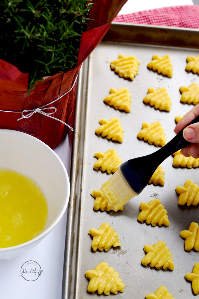 hand brushing egg wash on Christmas tree cookies on baking sheet