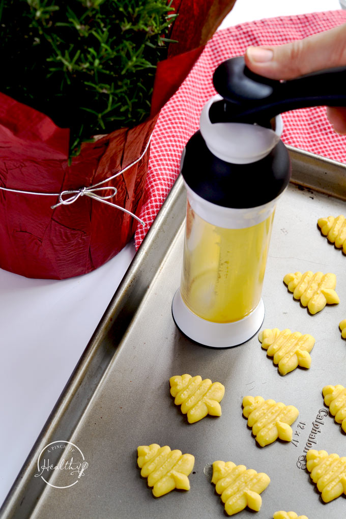 Pressing dough through a cookie press onto a baking sheet