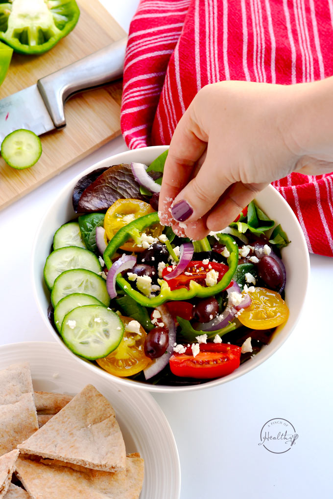 Woman's hand sprinkling feta cheese on a salad
