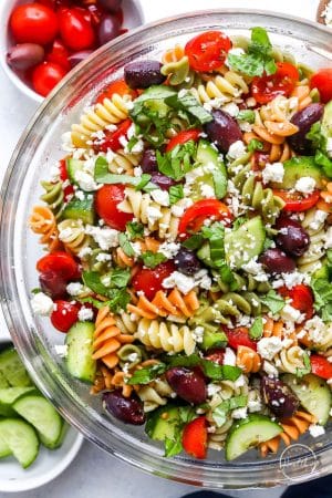 Closeup side shot tossed Greek Pasta Salad in glass bowl