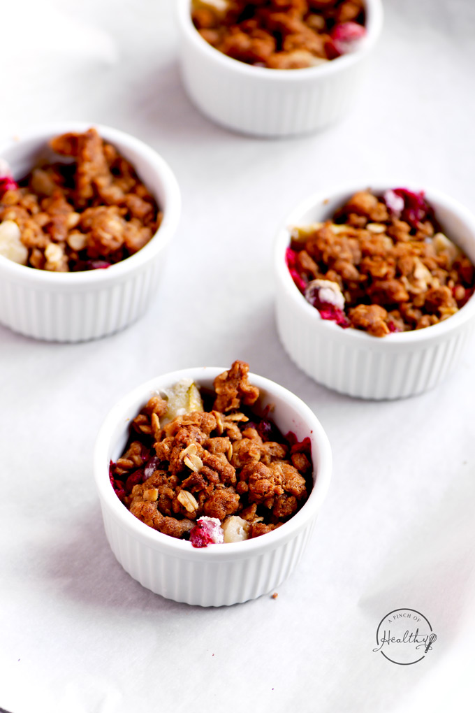 Individual fruit crisps in white ramekins on parchment lined baking sheet