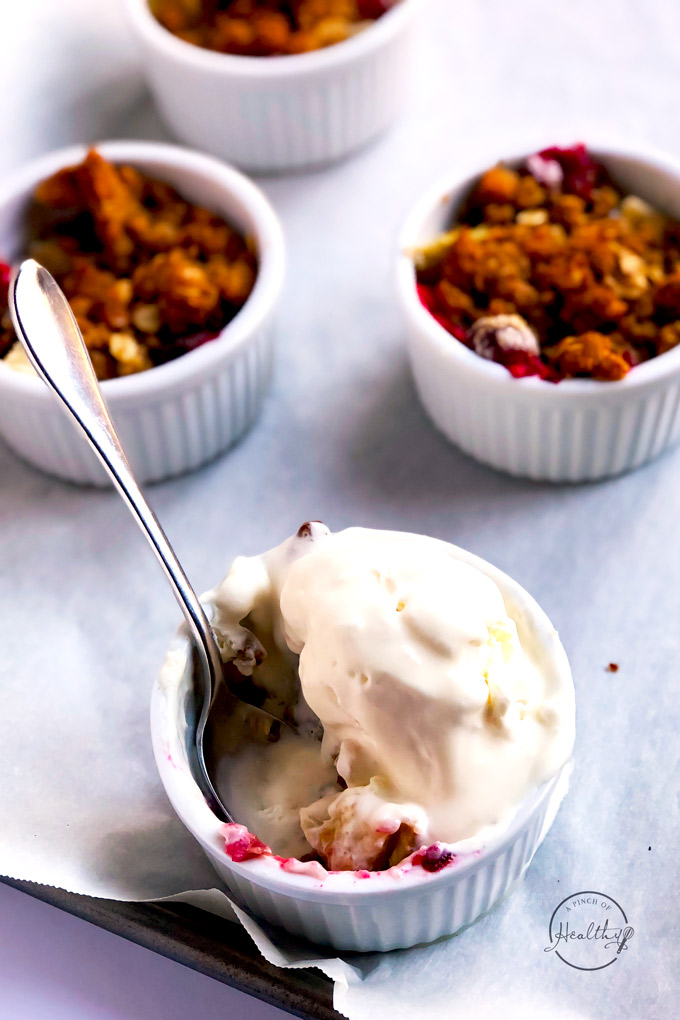 cranberry apple crisp a la mode with a spoon in individual ramekim