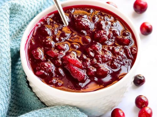 easy homemade cranberry sauce in a white bowl with spoon and blue towel