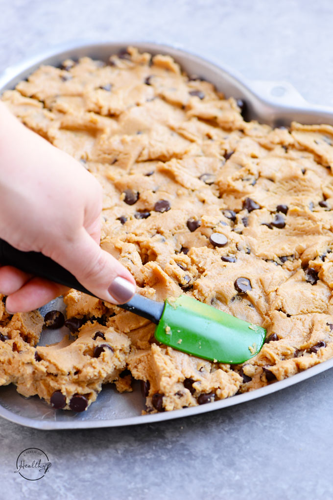 Pressing dough for peanut butter chocolate chip cookie cake into the prepared baking dish.