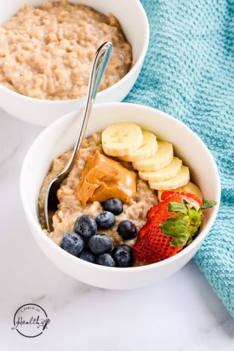 White bowl with oatmeal topped with peanut butter and berries, with a blue towel on the side