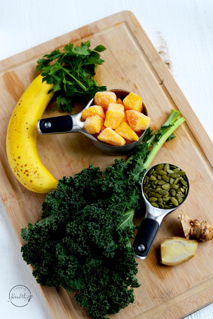 Immunity boosting smoothie ingredients - Kale, pumpkin seeds, mango, banana, ginger and parsley on wood cutting board