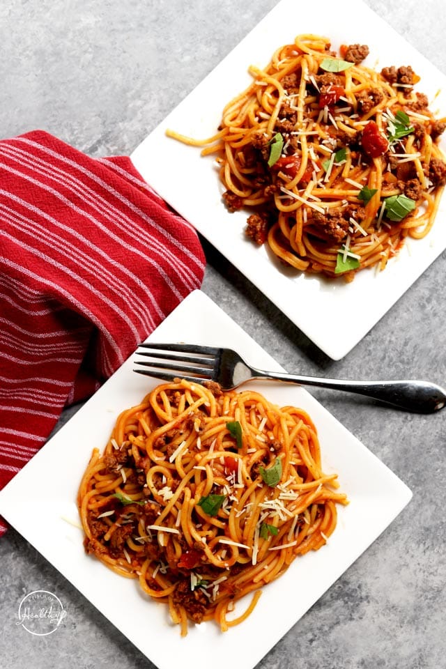 Spaghetti on square white plates overhead with red towel
