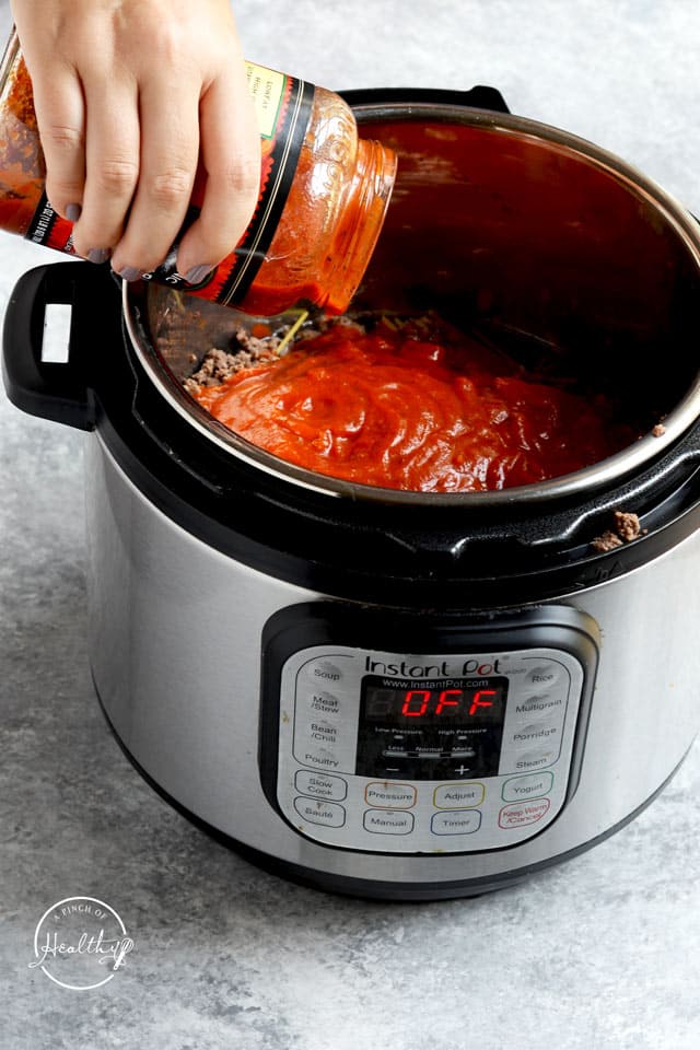 pouring pasta sauce into Instant Pot over ground beef