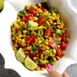 Corn salad with avocado and tomato in white bowl with lime slices