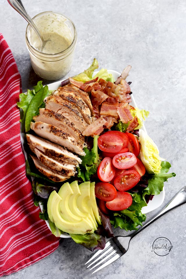 Chicken BLT salad overhead on a white plate with a jar of ranch dressing