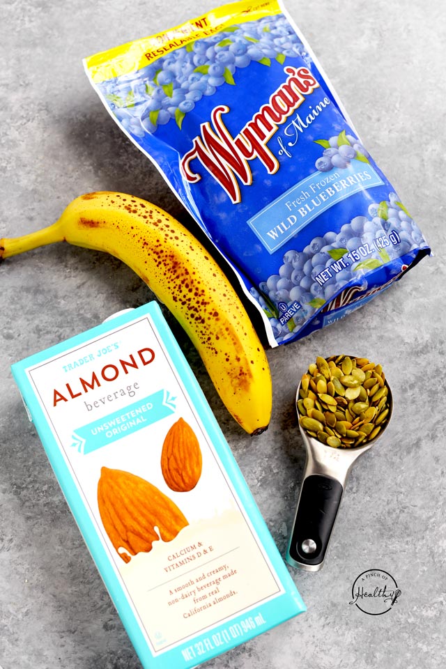Banana almond milk blueberries and pumpkin seeds on a gray background