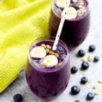 Blueberry smoothie with banana slices, blueberries and pumpkin seed on top and polka dot straws