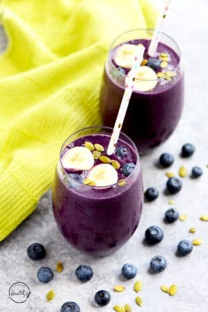 Blueberry smoothie with banana slices, blueberries and pumpkin seed on top and polka dot straws