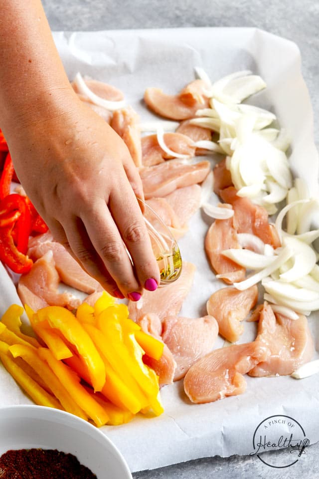 Drizzling oil on chicken and vegetables for sheet pan easy chicken fajitas