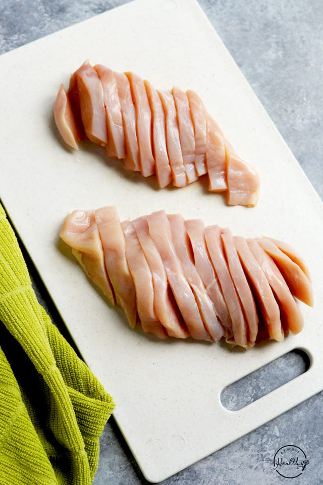 sliced raw chicken breasts on white cutting board