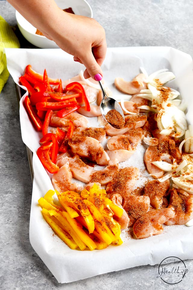 Sprinkling seasoning on easy chicken fajitas on a sheet pan