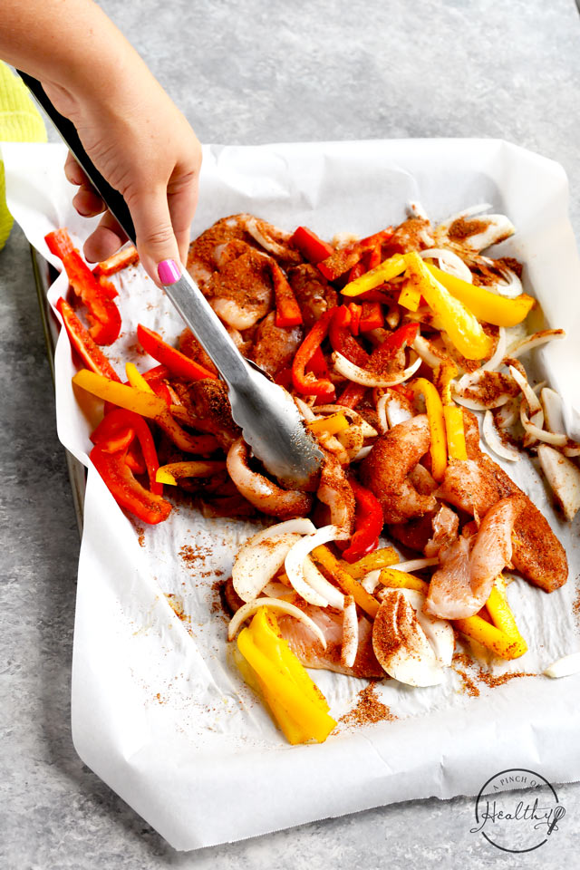 Tongs tossing ingredients for easy chicken fajitas on a sheet pan