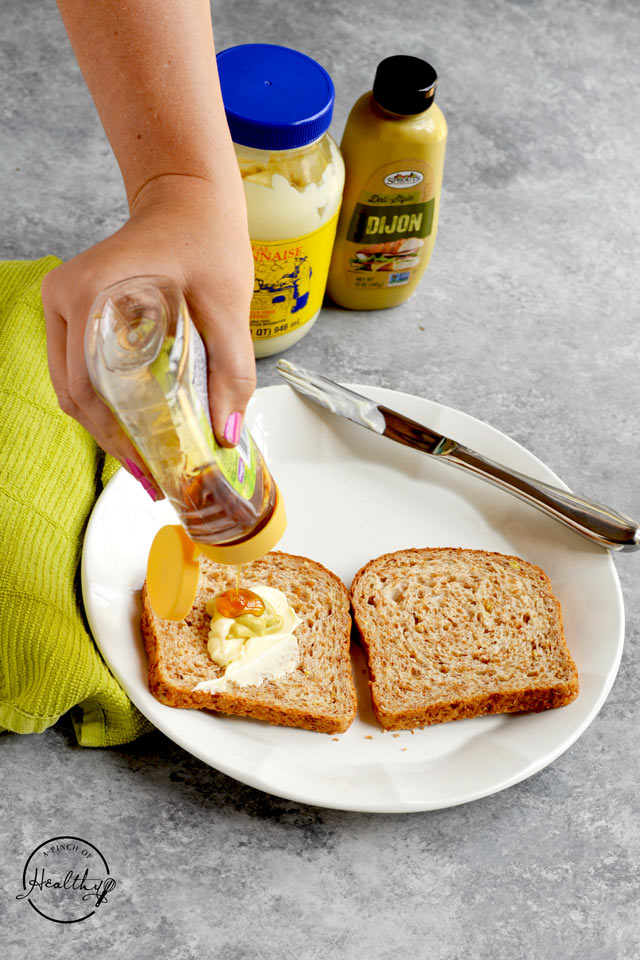 Squeezing honey on slice of bread with mayo and dijon mjustard