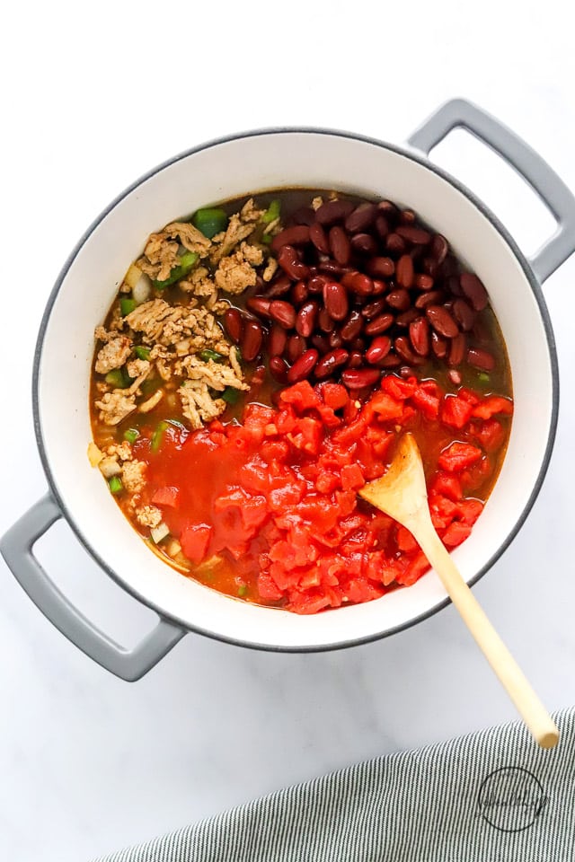 adding beans and tomatoes to meat in a pot