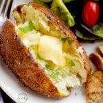 Air fryer baked potato with melted butter on a plate with chicken and salad