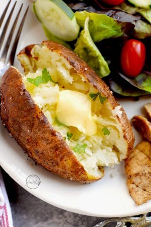 Air fryer baked potato with melted butter on a plate with chicken and salad