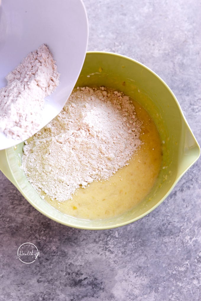 Adding dry ingredients to wet ingredients in a green bowl to make banana chocolate chip muffins